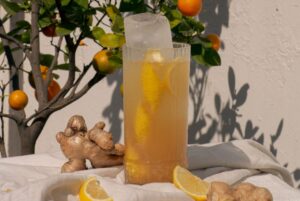 Rompe Mar Chilcano cocktail with ginger and lemon garnish on a white tablecloth with an orange tree and white wall in the background