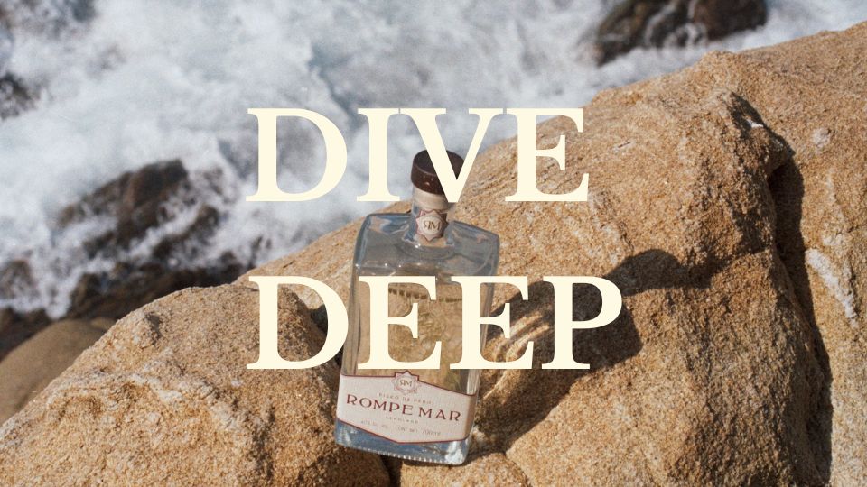 Rompe Mar bottle sitting on beach rock with ocean in background, 'Dive Deep' written in large letters