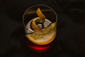 Rompe Mar Pisco Negroni cocktail with lemon garnish in a dark background