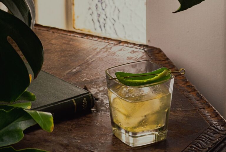 Rompe Mar cocktail Reyes on wood table with Monstera leaves and book